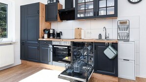 Une cuisine moderne avec des meubles de couleur sombre, un lave-vaisselle, une machine à café et une horloge murale.