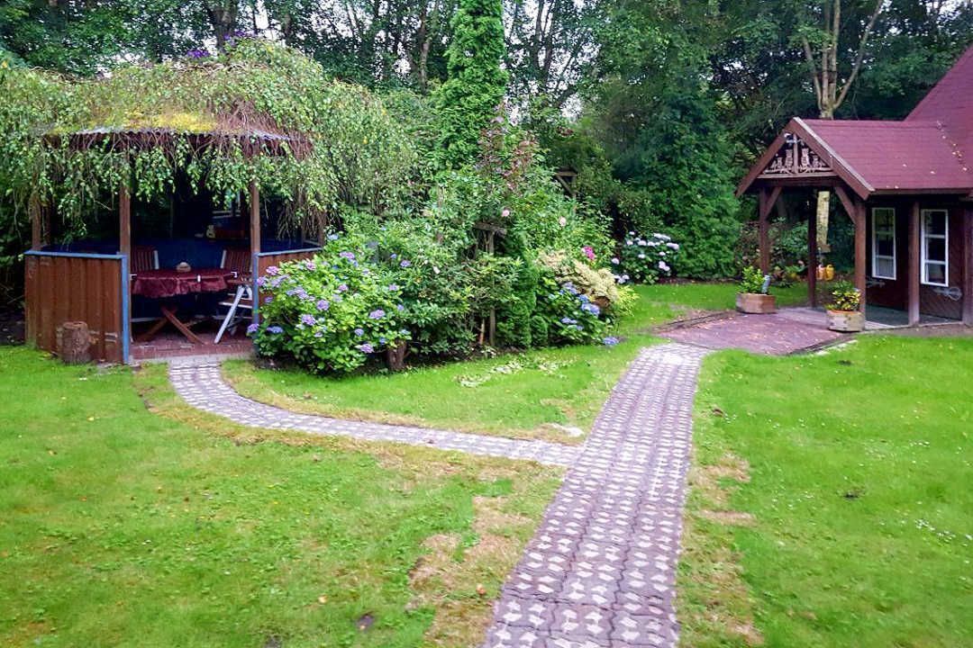 A garden with a gazebo, a wooden structure, and a pathway leading to a building.