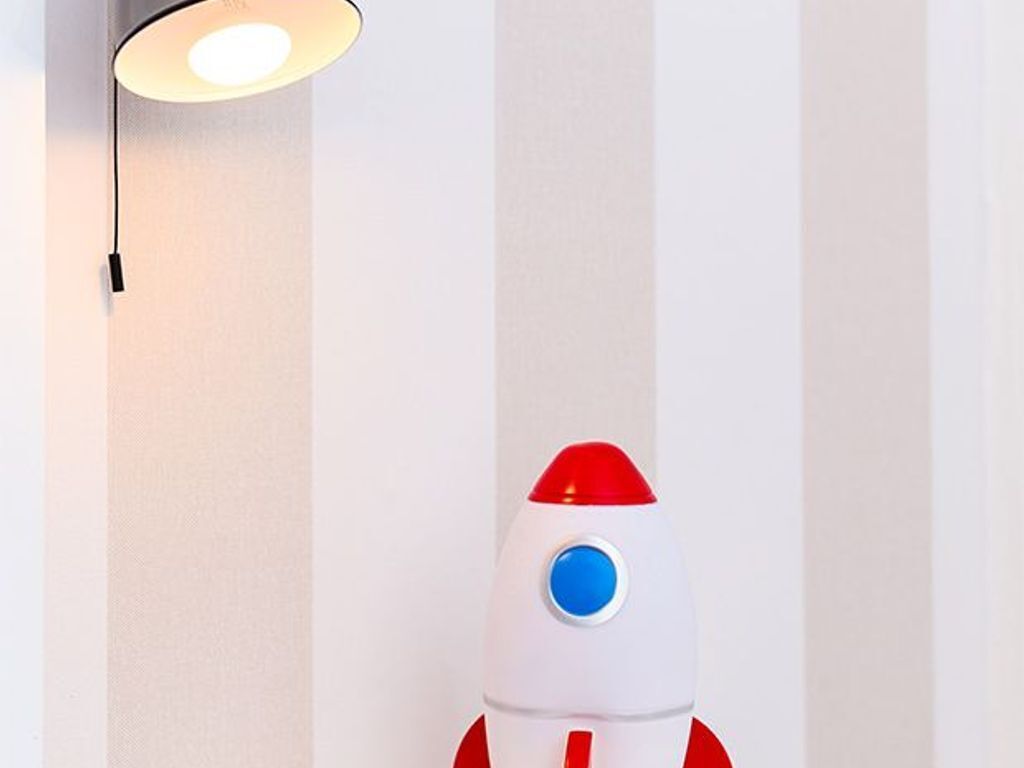 A toy rocket against a striped wall with a light fixture above it.