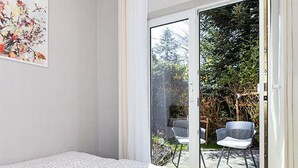 Une chambre à coucher avec un lit et une porte-fenêtre coulissante donnant sur un espace extérieur aménagé avec des chaises.