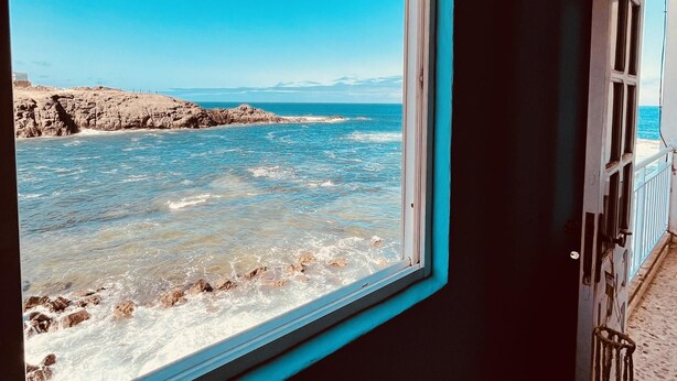 A window view of a rocky coastline with waves crashing against the shore. - Casa Azul Holiday Home (El Cotillo)