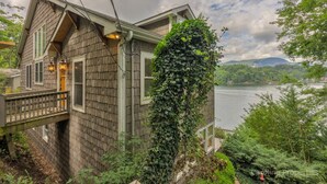 Ein Holzhaus mit Balkon und Blick auf einen See, umgeben von viel Grün.