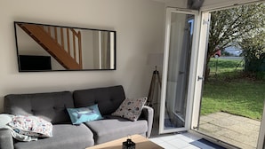 A living room with a grey sofa, patterned cushions, a wooden coffee table, and a sliding glass door leading to a garden. - Villa proche de la mer (Concarneau)
