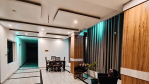 A modern hotel lobby with a reception desk, a dining area with chairs and a table, and a large window with curtains. - Golden Rock - AM Hotel Kollection (Dharamshala)