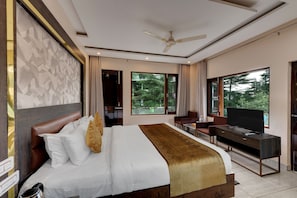 A modern hotel room with a large bed, a desk with a flat-screen TV, and a view of the outdoors. - Golden Rock - AM Hotel Kollection (Dharamshala)