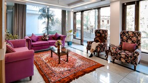 A modern living room with a purple sofa, floral armchairs, and a patterned rug. - Golden Rock - AM Hotel Kollection (Dharamshala)