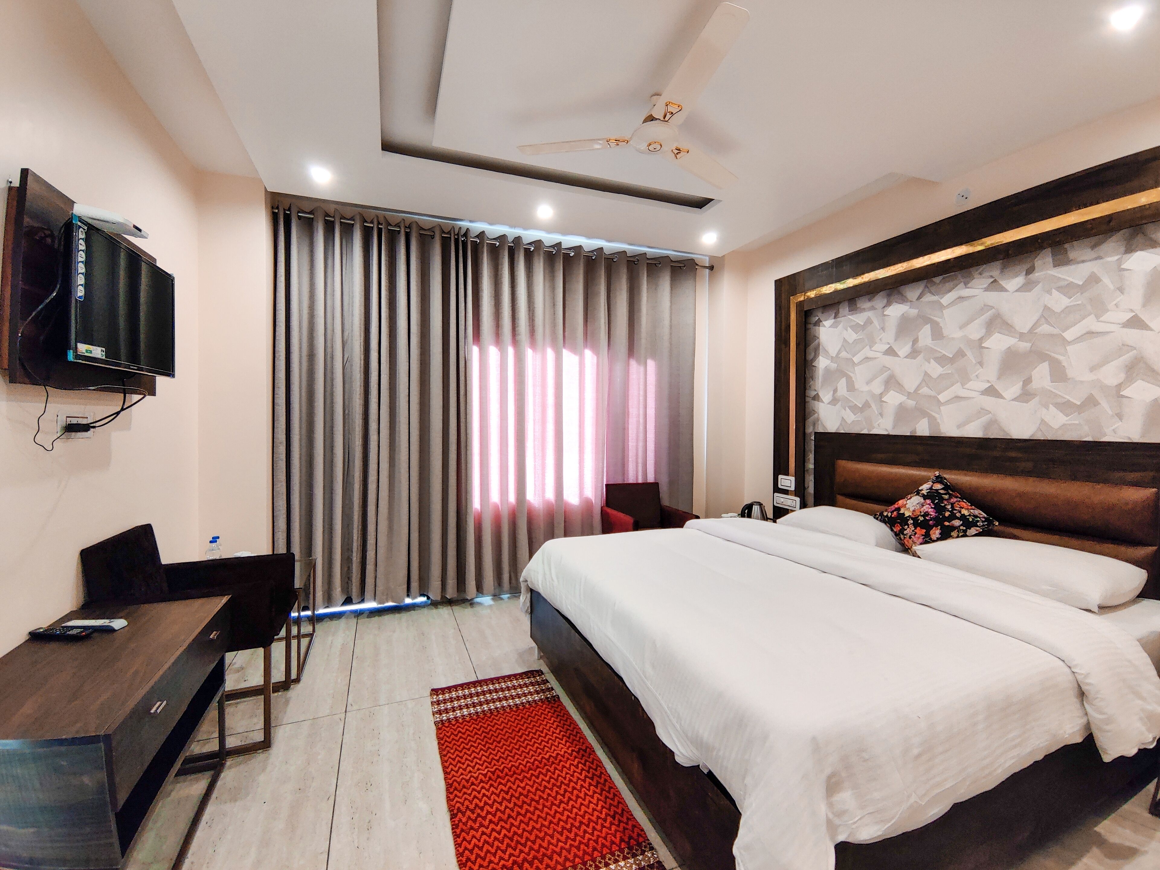 A hotel room with a bed, a desk, a TV, and curtains.