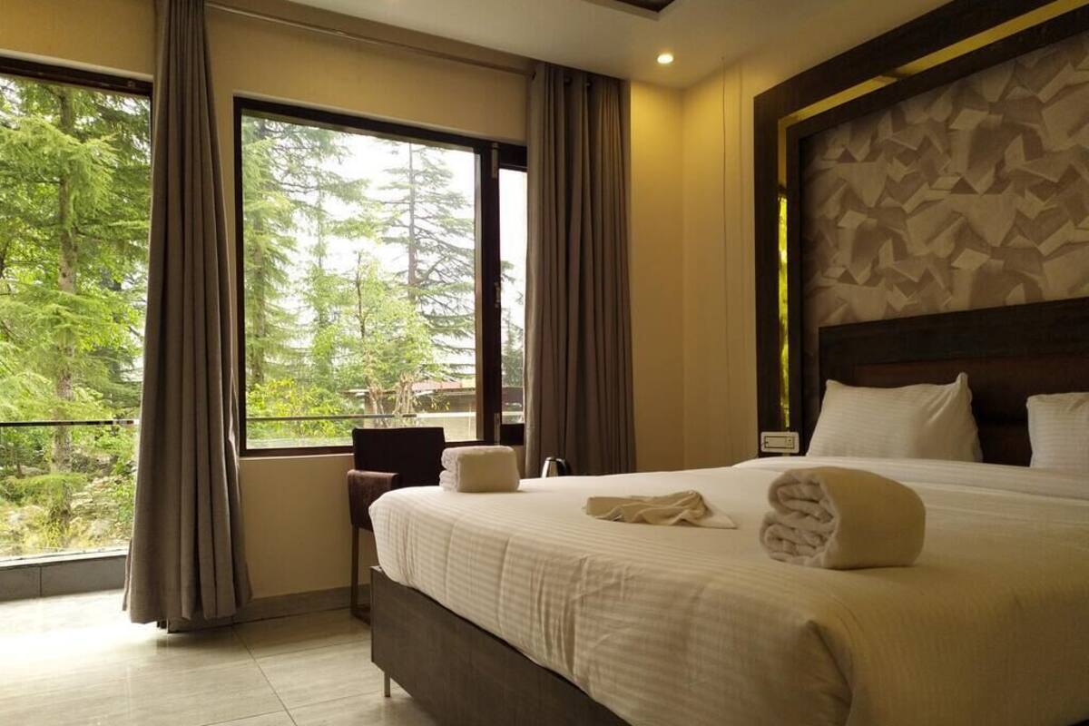 A hotel room with a large bed, a view of trees through the window, and a modern design.