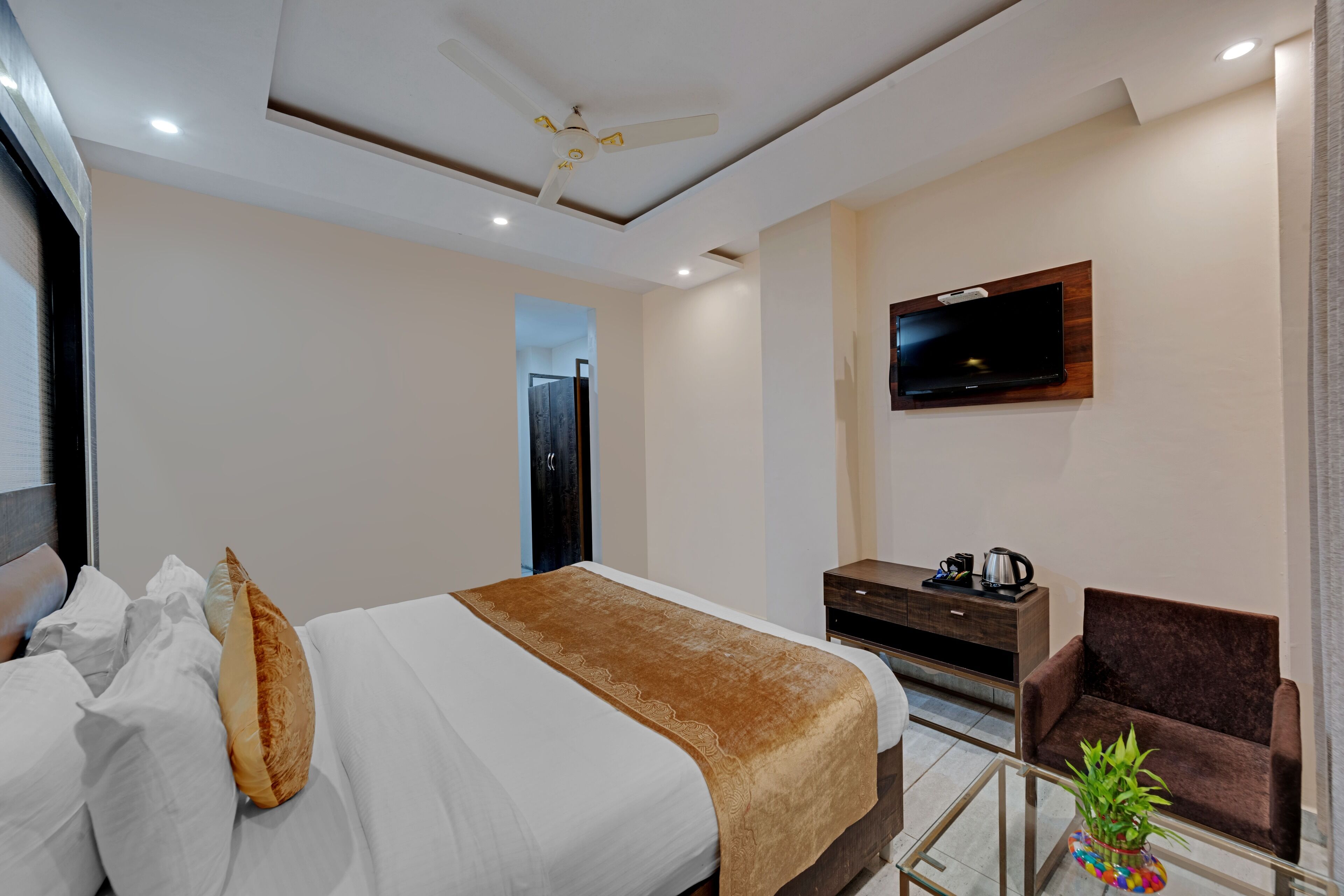 Quarto de hotel moderno com uma cama grande, televisão na parede, escrivaninha, cadeira e uma pequena planta.