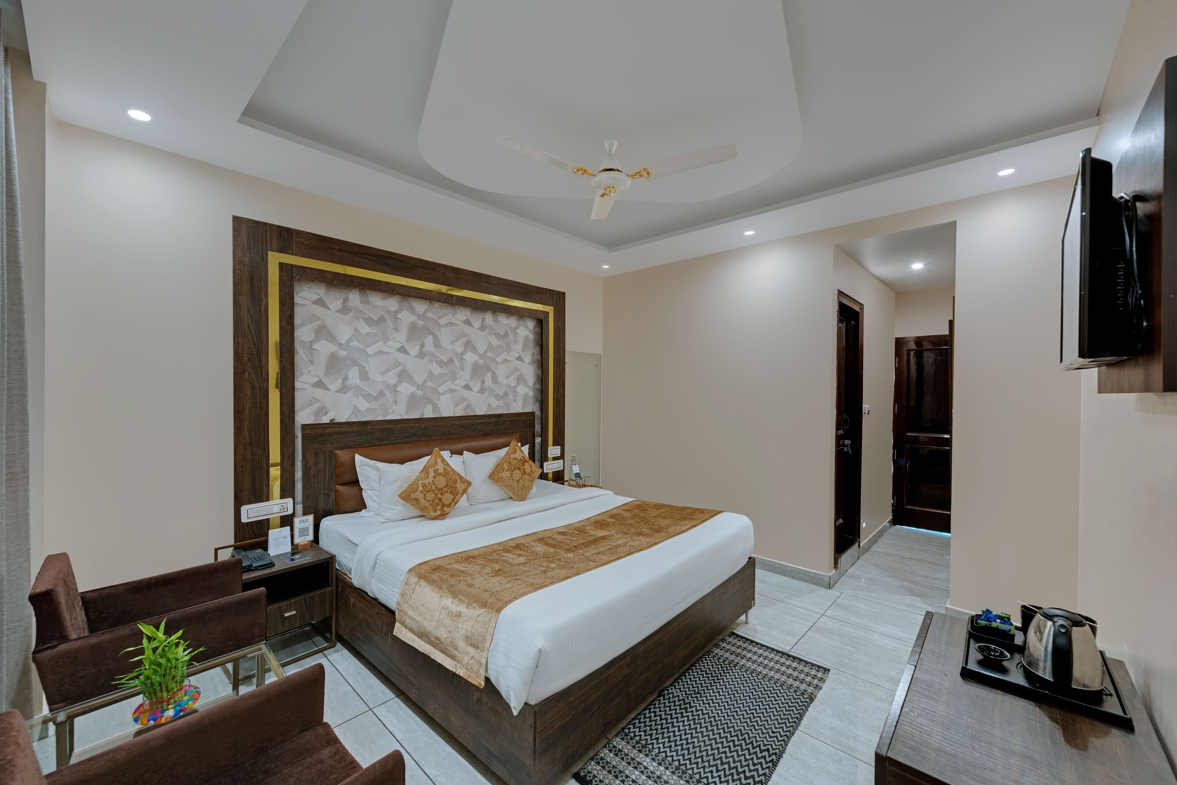 A hotel room with a large bed, a desk with a chair, a TV mounted on the wall, and a ceiling fan.