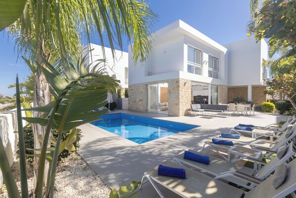 Une maison moderne dotée d’une piscine, de chaises longues et d’un espace patio.