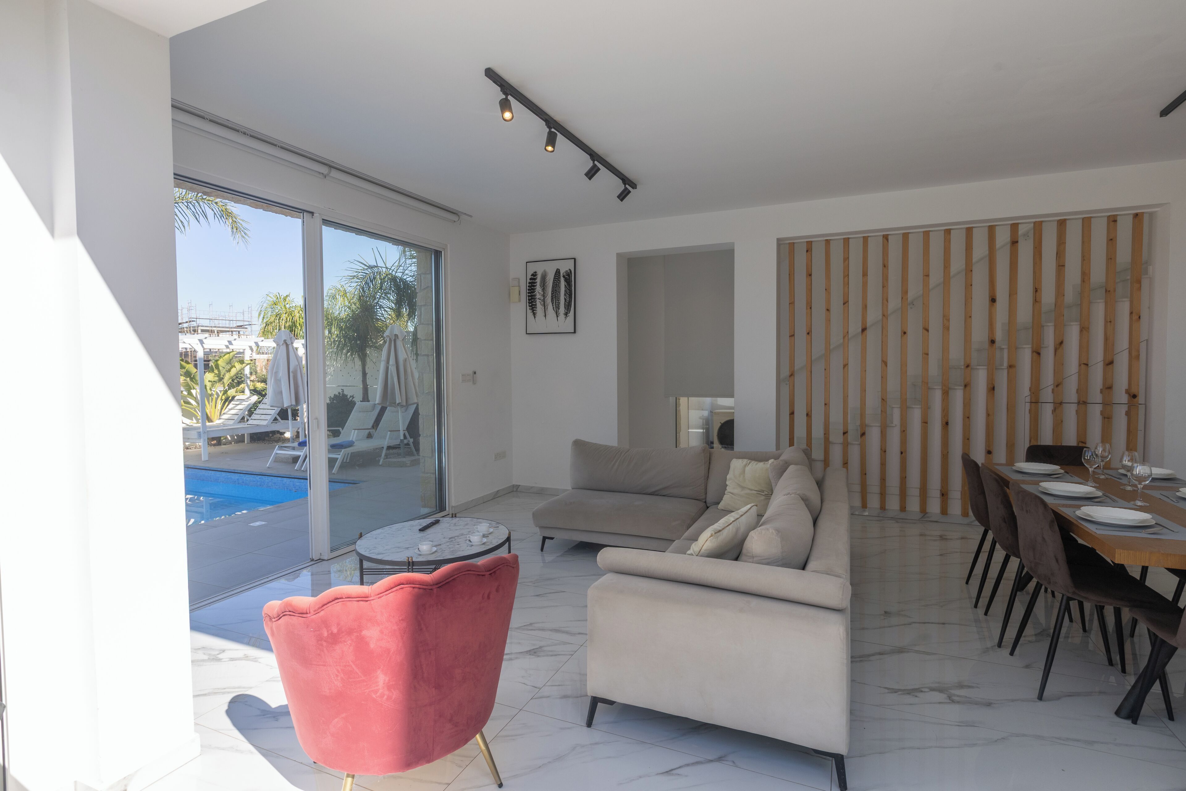 A modern living space with a pool, a sofa, a dining area, and a large sliding glass door leading to the pool.