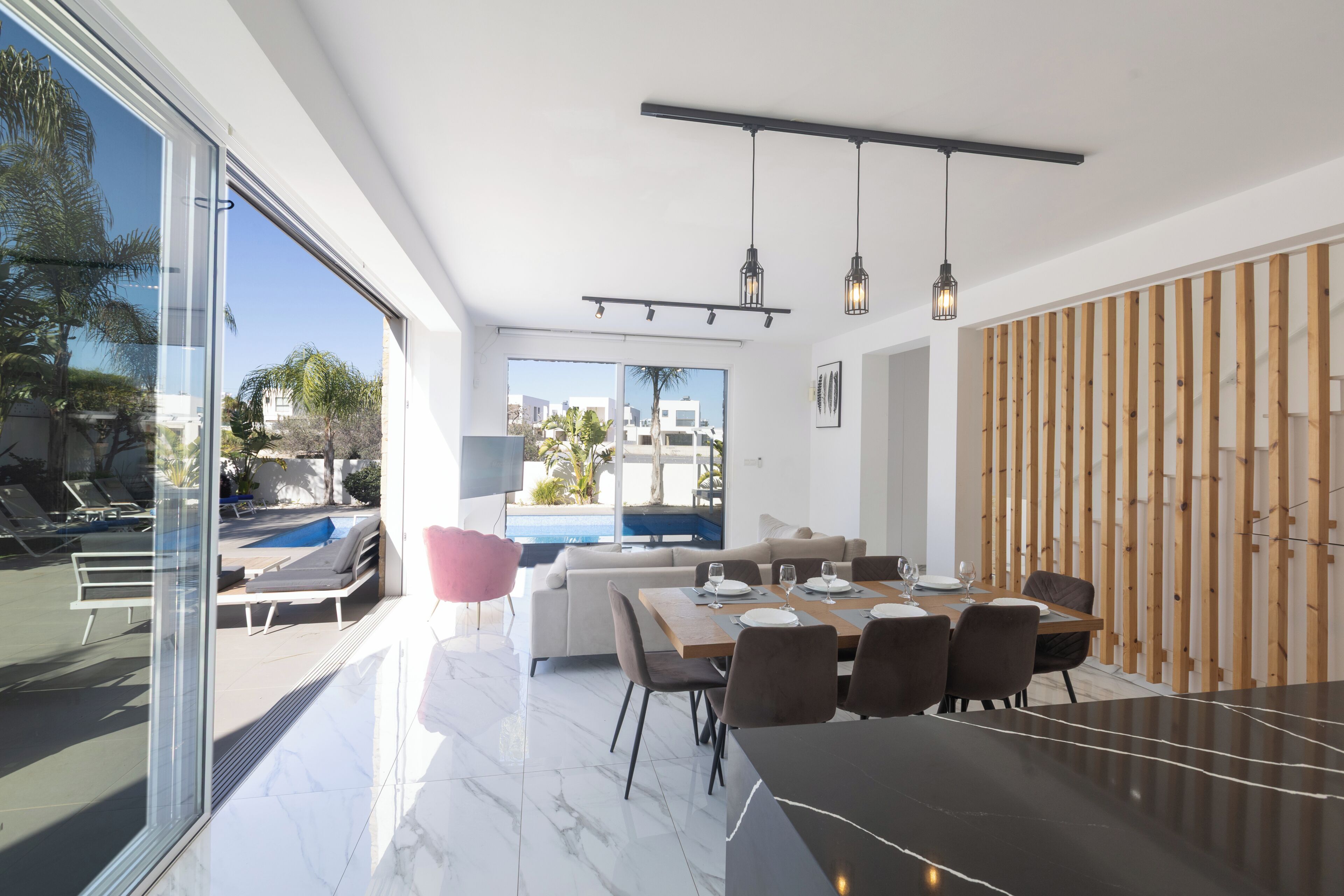 A modern dining area with a large table, chairs, and pendant lights.