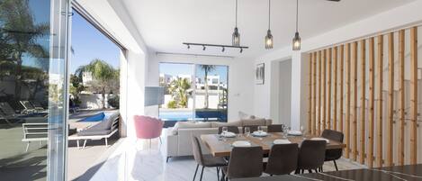 A modern dining area with a large table, chairs, and pendant lights.