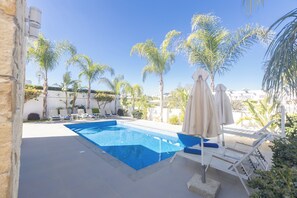 Une piscine entourée de palmiers et d’un moulin à vent, avec des chaises longues et des parasols à proximité.