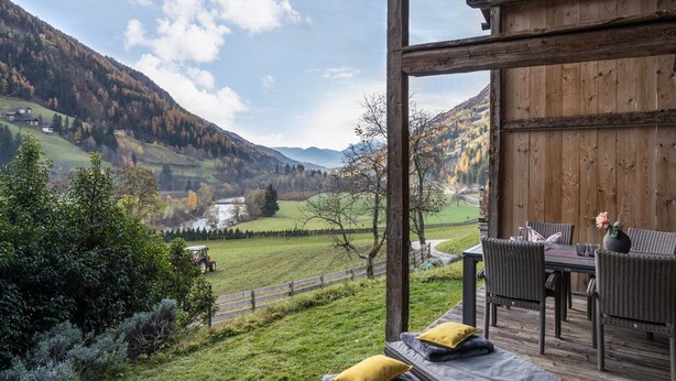 A wooden deck with a table and chairs, overlooking a valley with houses and mountains. - Chalet 'Ferienhaus Im Stadl' with Mountain Views, Private Terrace and Wi-Fi (St. Martin in Passeier)