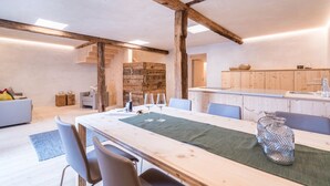 A modern kitchen with wooden beams, a dining area with a long table, and a cozy seating arrangement. - Chalet 'Ferienhaus Im Stadl' with Mountain Views, Private Terrace and Wi-Fi (St. Martin in Passeier)