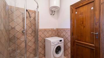 A bathroom with a glass shower enclosure, a washing machine, and a wooden door.