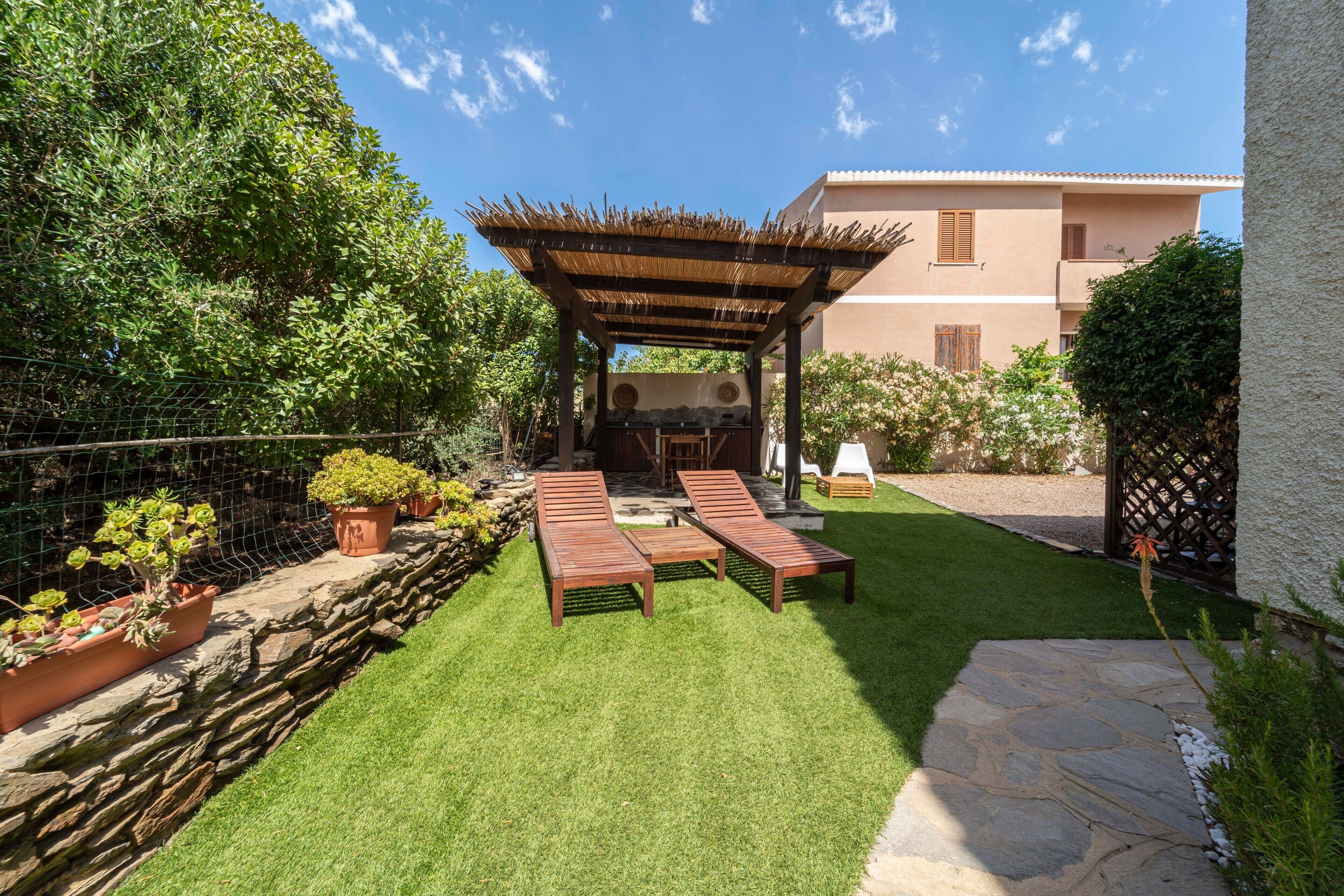 Un patio con lettini in legno, un pergolato e un vialetto in pietra.