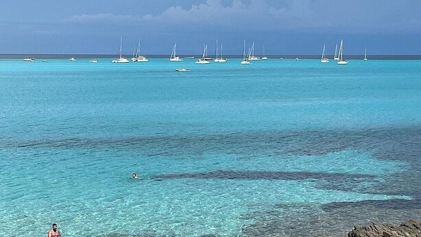 Eine Küstenlandschaft mit klarem türkisblauem Wasser, Booten und einer felsigen Küste.