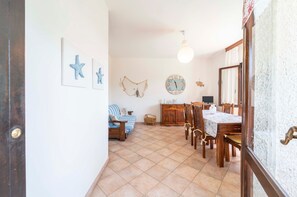 A dining area with a wooden table and chairs, a clock on the wall, and a sofa in the background.