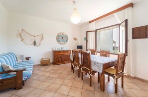 A dining area with a wooden table and chairs, a sofa, a clock, and a hanging net decoration.