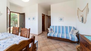 Ein Zimmer mit einem Holzespeisetisch, Stühlen, einer gestreiften Couch, einer Deckenleuchte und einer an der Wand befestigten Ziernetzdeko.