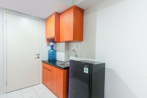 Une cuisine avec des meubles de rangement en bois, un réfrigérateur noir, un distributeur d’eau bleu et une porte blanche.
