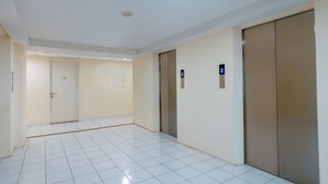 A hallway with white tiled floors, beige walls, and two elevators. - Life 2837 Apartment Dramaga Tower (Dramaga)