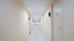 A long, narrow hallway with white tiled floors and cream-colored walls, leading to a door at the end. - Life 2837 Apartment Dramaga Tower (Dramaga)