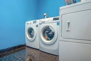 A laundry area with two front-loading washing machines and a dryer, a blue wall, and a marble floor. - Life 2837 Apartment Dramaga Tower (Dramaga)