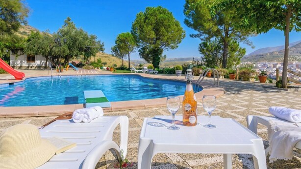 A poolside area with lounge chairs, a bottle of wine, and a view of the surrounding landscape. - La Guitarra Andaluza Loja by Ruralidays (Granada)