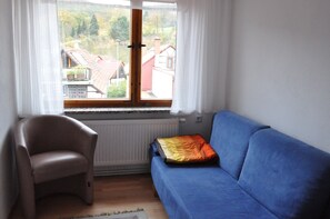 Una habitación con un sofá azul, un sillón beige y una ventana con cortinas.