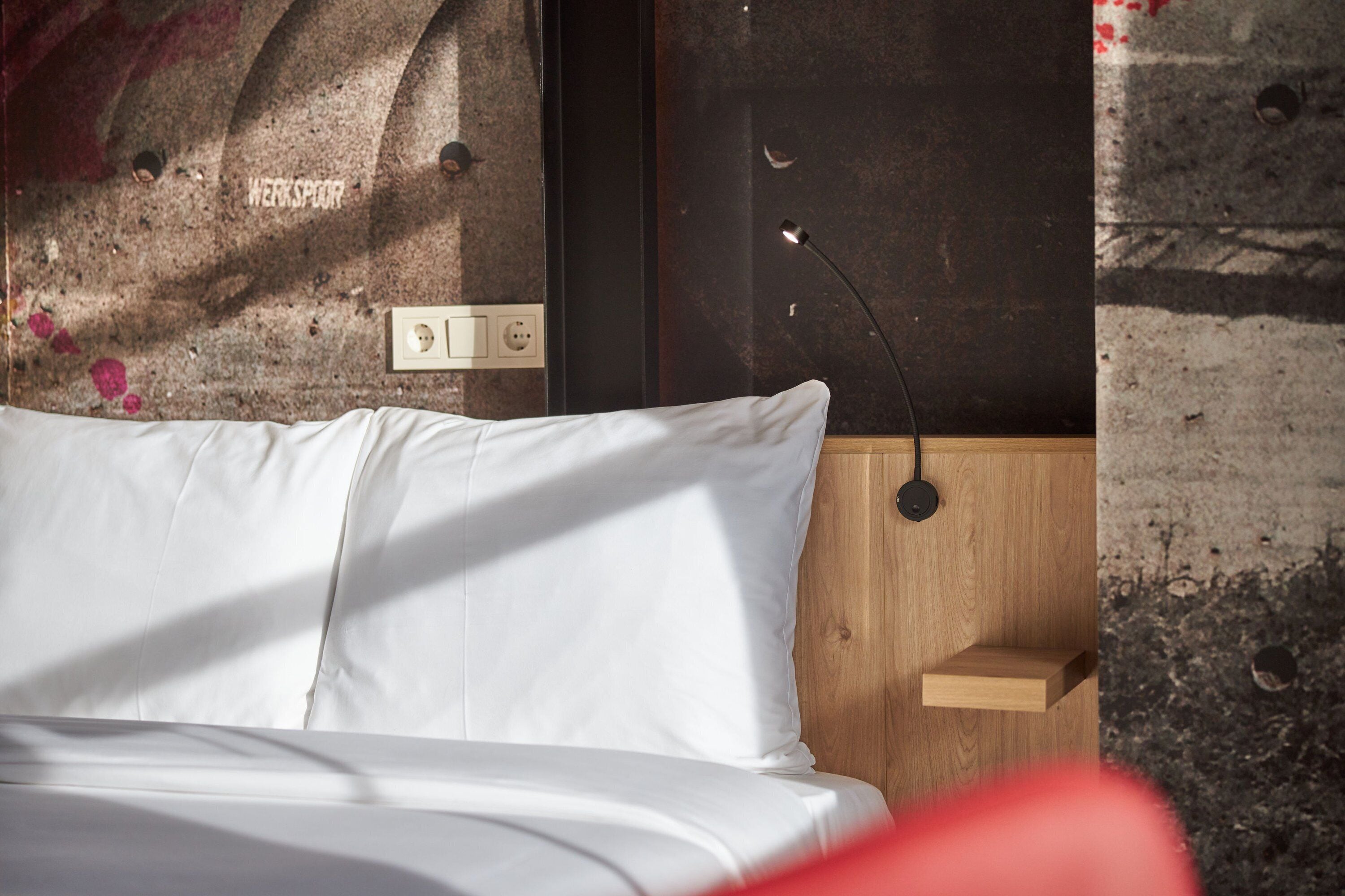 A bed with white bedding, a wooden headboard, and a wall with a textured surface and a small shelf.