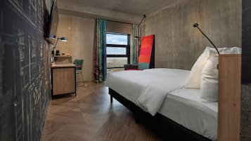 Una habitación de hotel moderna con una cama grande, un escritorio, una silla y vistas a la ciudad por la ventana.