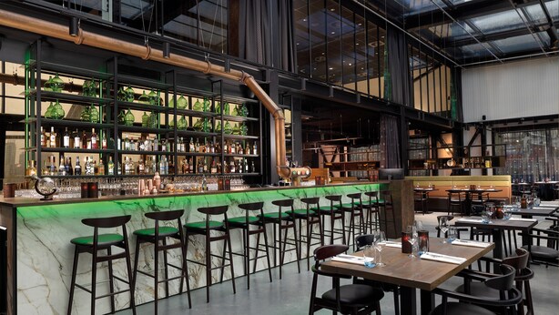 Un espace bar doté d’un comptoir en marbre vert, de plusieurs tabourets et d’une variété de bouteilles et de verres.