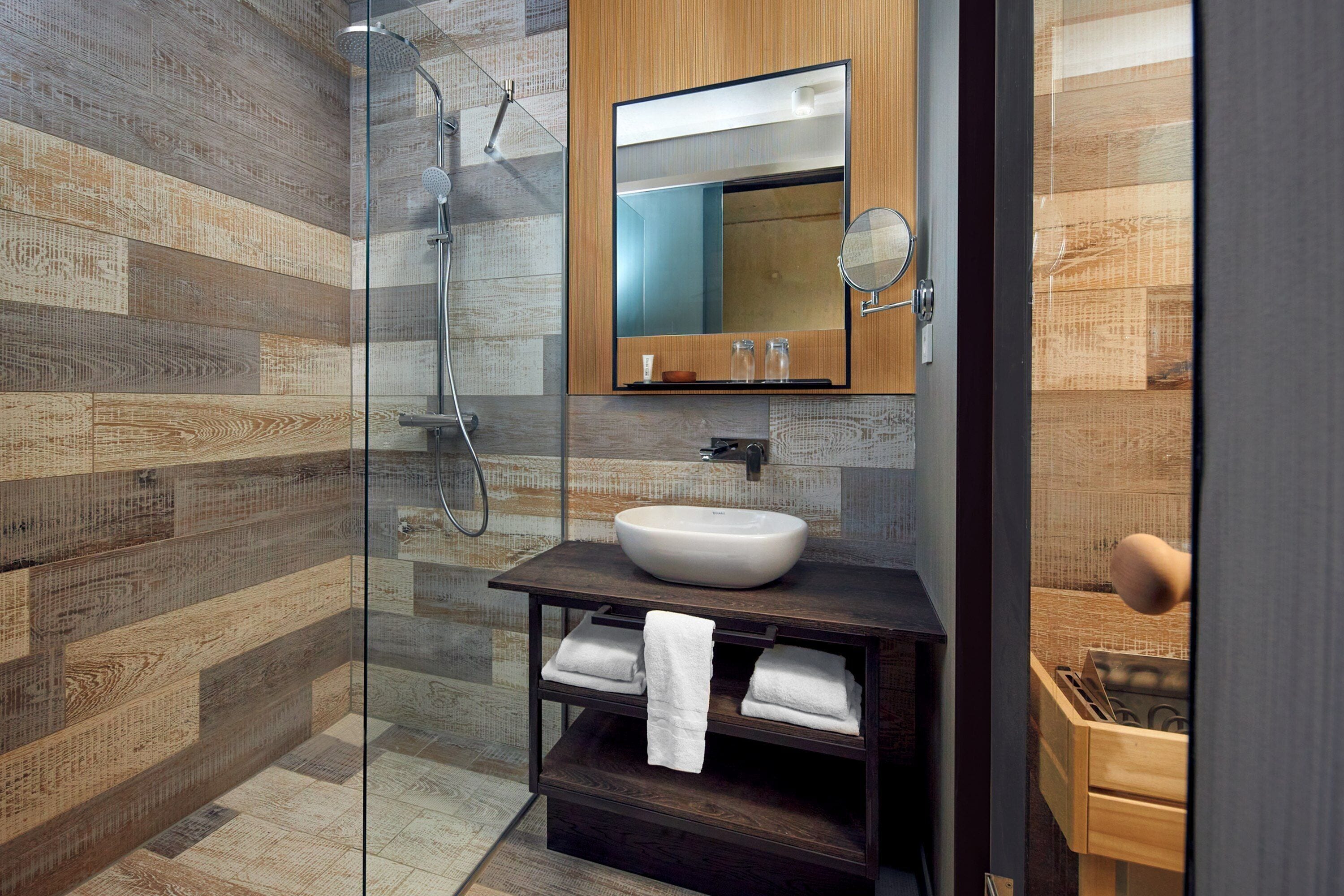 Un bagno moderno con cabina doccia in vetro, mobile bagno in legno con lavabo a incasso e uno specchio grande sopra il lavabo.