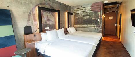 Habitación de hotel con una cama grande, una pequeña mesa redonda, un banco y una pared con un cartel antiguo.