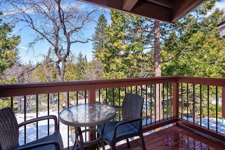 A covered outdoor area with a wooden deck, a glass table, and two chairs.. (B208) Loft Condominiums