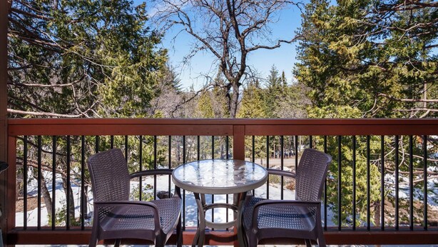 A balcony with two chairs and a glass table, overlooking a snowy landscape with trees.