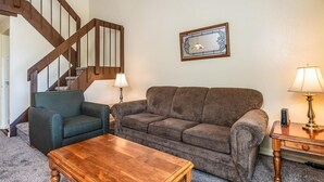 A living room with a wooden staircase, a green armchair, a brown sofa, a wooden coffee table, and a framed picture on the wall.