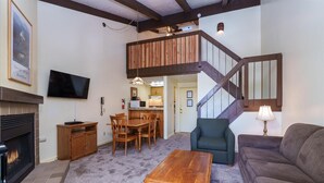 A living room with a fireplace, a dining area, a staircase, and a kitchen in the background.