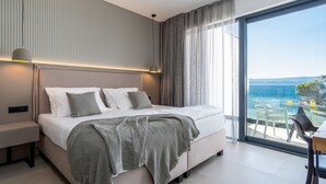 Een moderne slaapkamer met een groot bed, een nachtkastje, een lamp en uitzicht op zee door een groot raam.