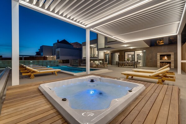 A modern outdoor pool area with a hot tub, lounge chairs, and a covered patio.