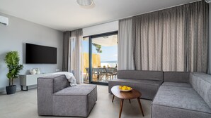 Een moderne woonkamer met een grijze hoekbank, een klein voetenbankje, een houten salontafel met een fruitschaal, een flatscreen-televisie en een potplant.