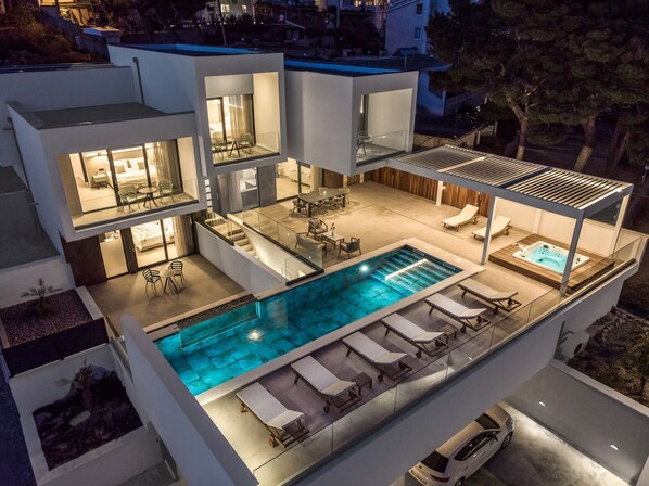 Une maison moderne à plusieurs étages, dotée d’une piscine sur le toit, d’un espace extérieur aménagé et d’un intérieur bien éclairé.