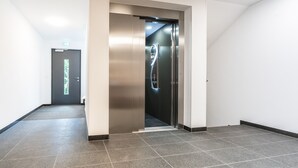 A modern elevator with a metallic finish, a tiled floor, and a plain wall. - Prim Loge (Balgheim)
