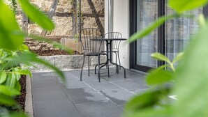 An outdoor patio with a stone wall, a metal table and chairs, and a glass door. - Prim Loge (Balgheim)