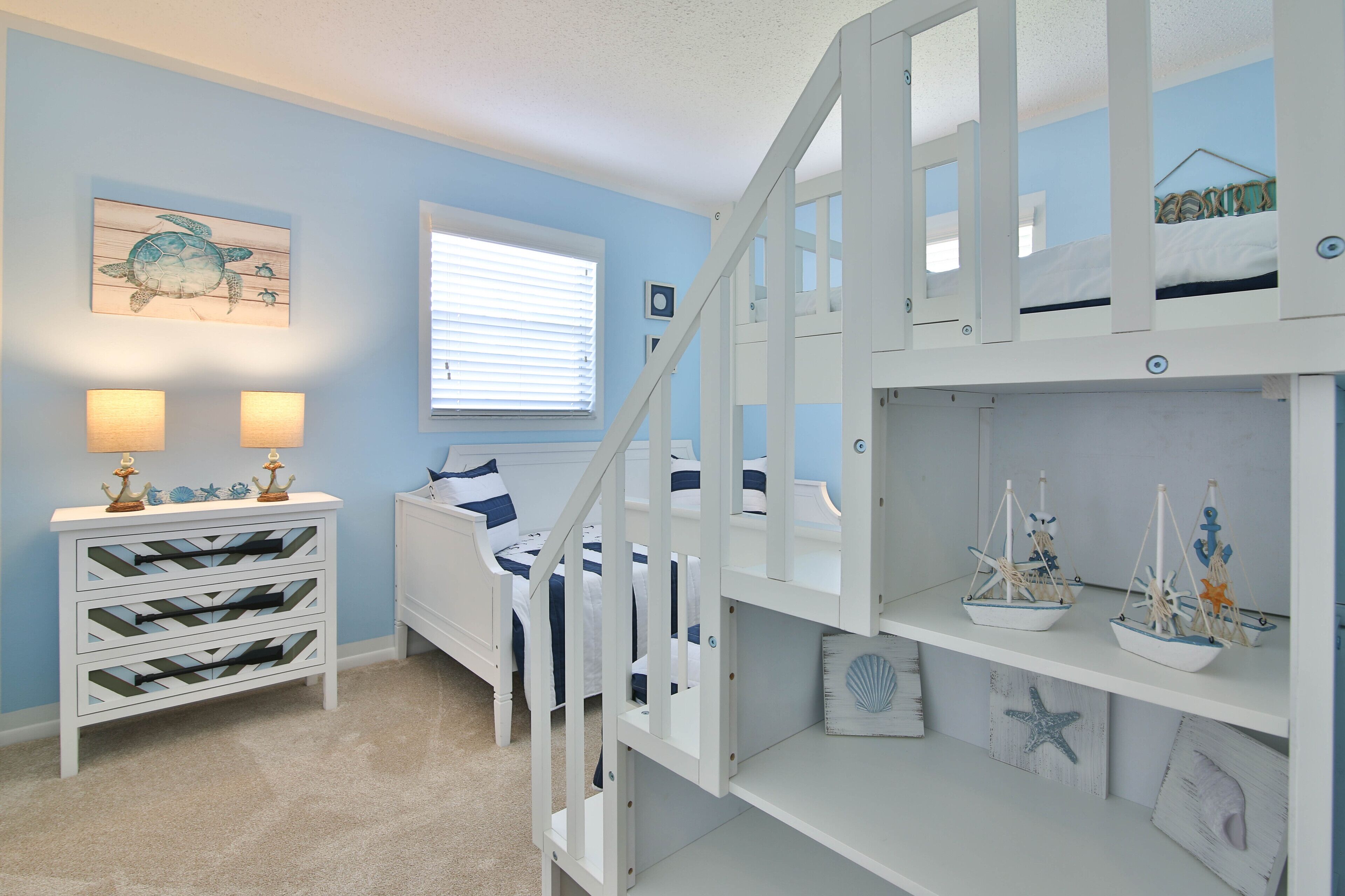 A bedroom with a bunk bed, a dresser with drawers, a window with blinds, and nautical-themed decorations.