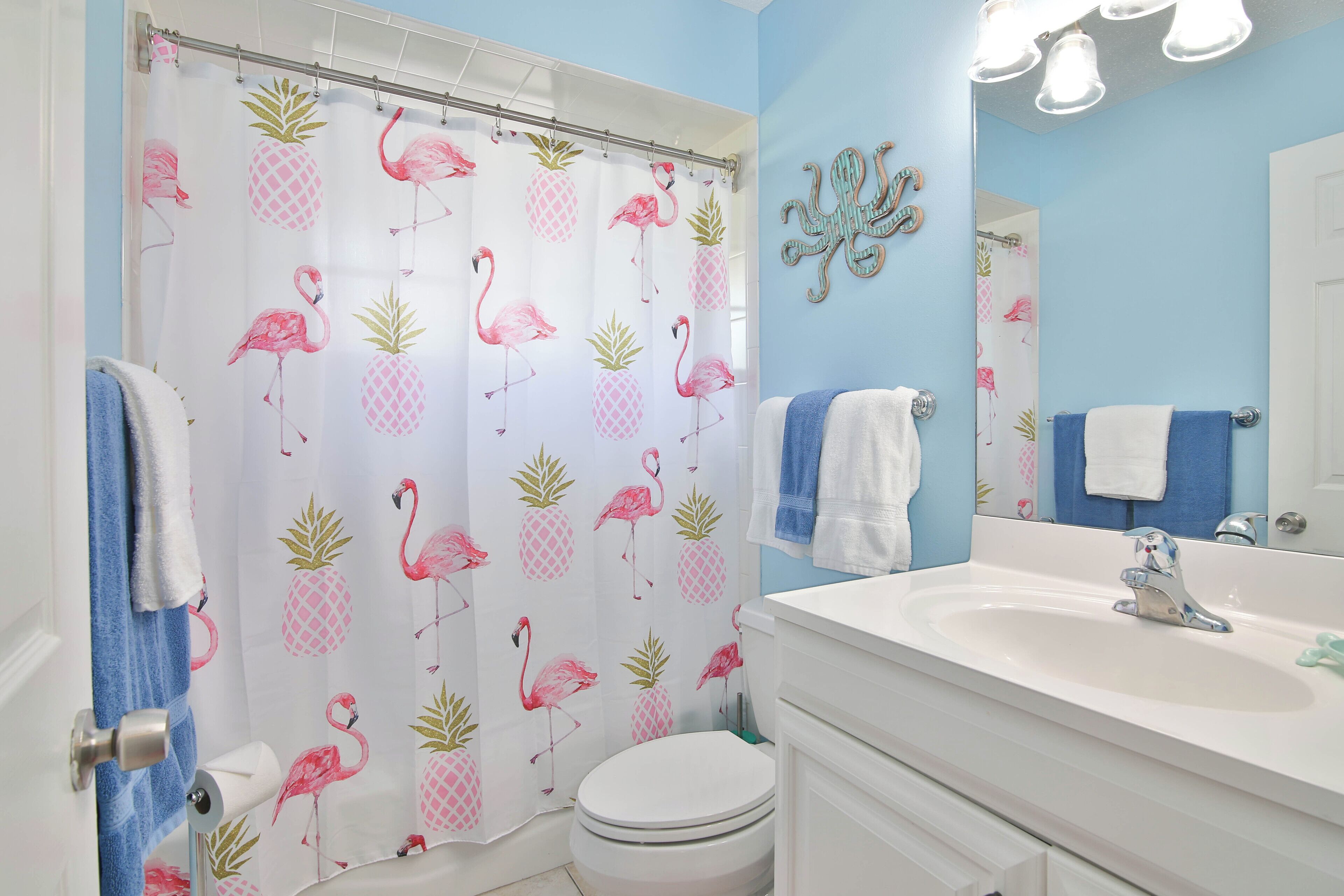 Ein Badezimmer mit Duschvorhang mit Flamingos und Ananas, einem weißen Waschbecken und einem Spiegel.